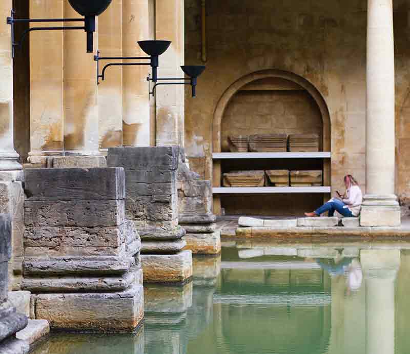 Woman sat against a Roman pillar by the waters.